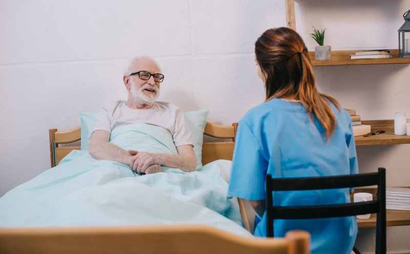 Smiling old patient in bed talking to nurse